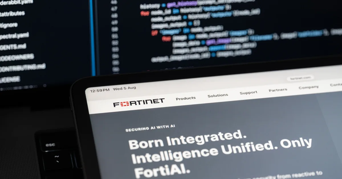 Tablet showing the Fortinet website in front of a blurred monitor displaying source code